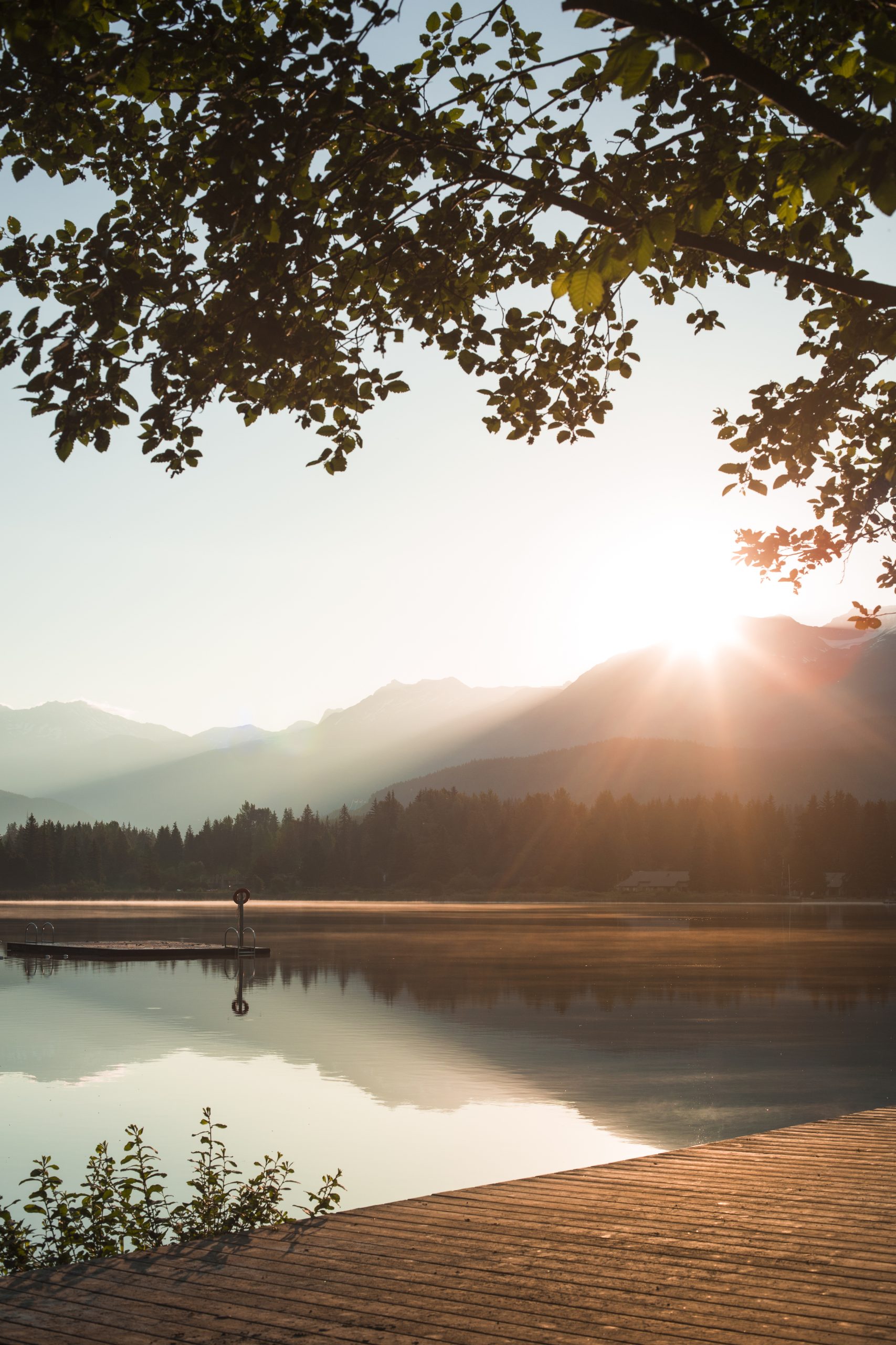 Sun peaking from being mountain and reflecting in calm lake.